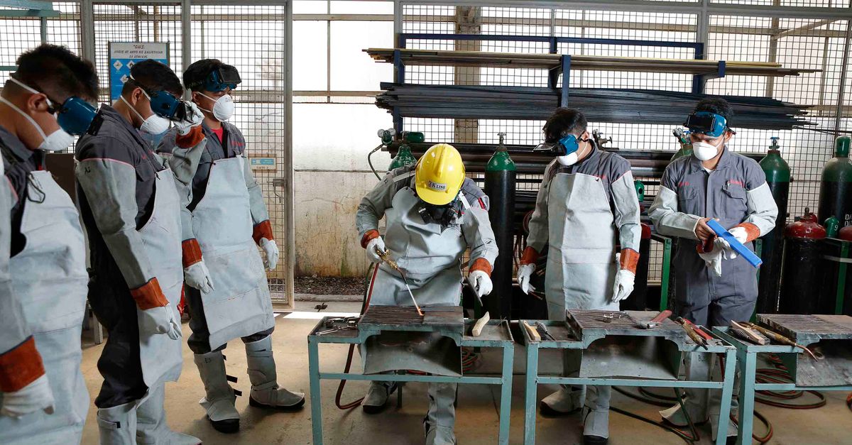 Workers in hard hats and protective gear during a hands-on training session on a factory floor.