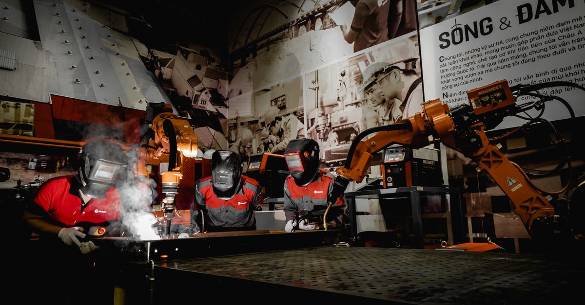 Three welders in protective gear working alongside robots in an industrial workshop
