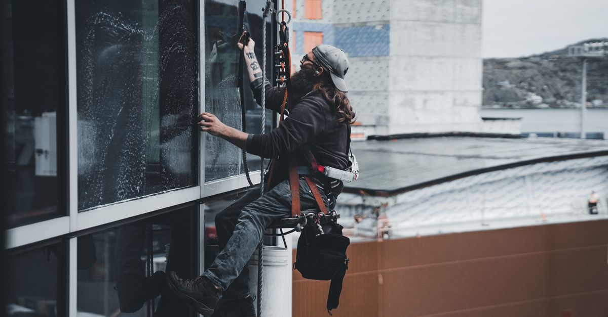 A worker in a safety harness cleaning the glass windows of a high-rise building
