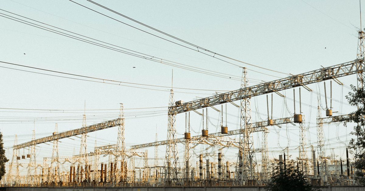 Wide view of an electrical substation with power lines and steel towers outdoors.