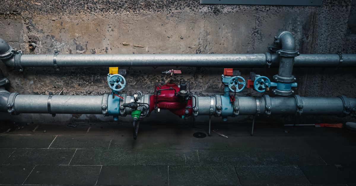 Industrial pipes with coloured valves running across a textured concrete wall.