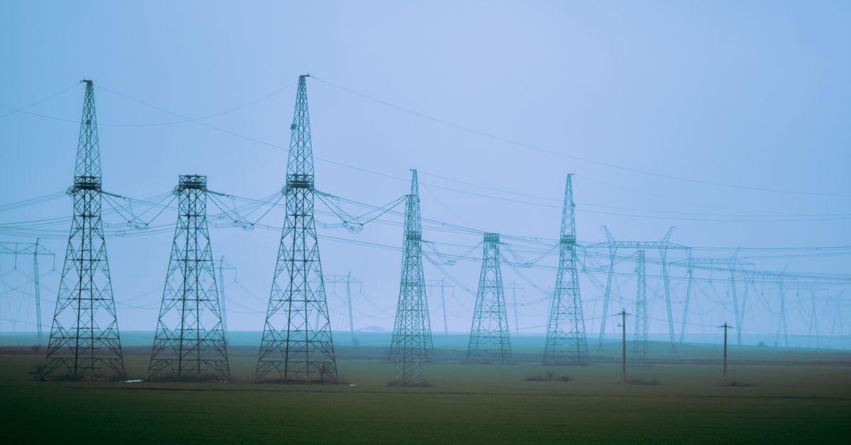 Rows of transmission towers and curved overhead wires at a station in a green field